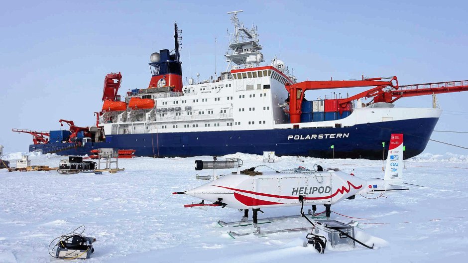 Foto: Falk Pätzold / TU Braunschweig zur Vergrößerungsansicht des Bildes: Das Foto zeigt eine die Hubschrauberschleppsonde HELiPOD stehend auf dem schneebedecktem Meereis. Im Hintergrund ist das Forschungsschiff Polarstern zu sehen. Foto: Falk Pätzold / TU Braunschweig