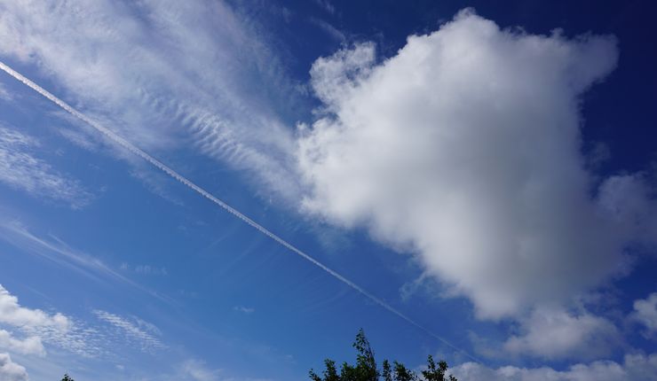 Neben einer Cumuluswolke sind die hohen Eiswolken, die Zirren zu sehen. Darunter ist auch eine linienförmige Zirruswolke, ein Kondensstreifen von einem Flugzeug. 