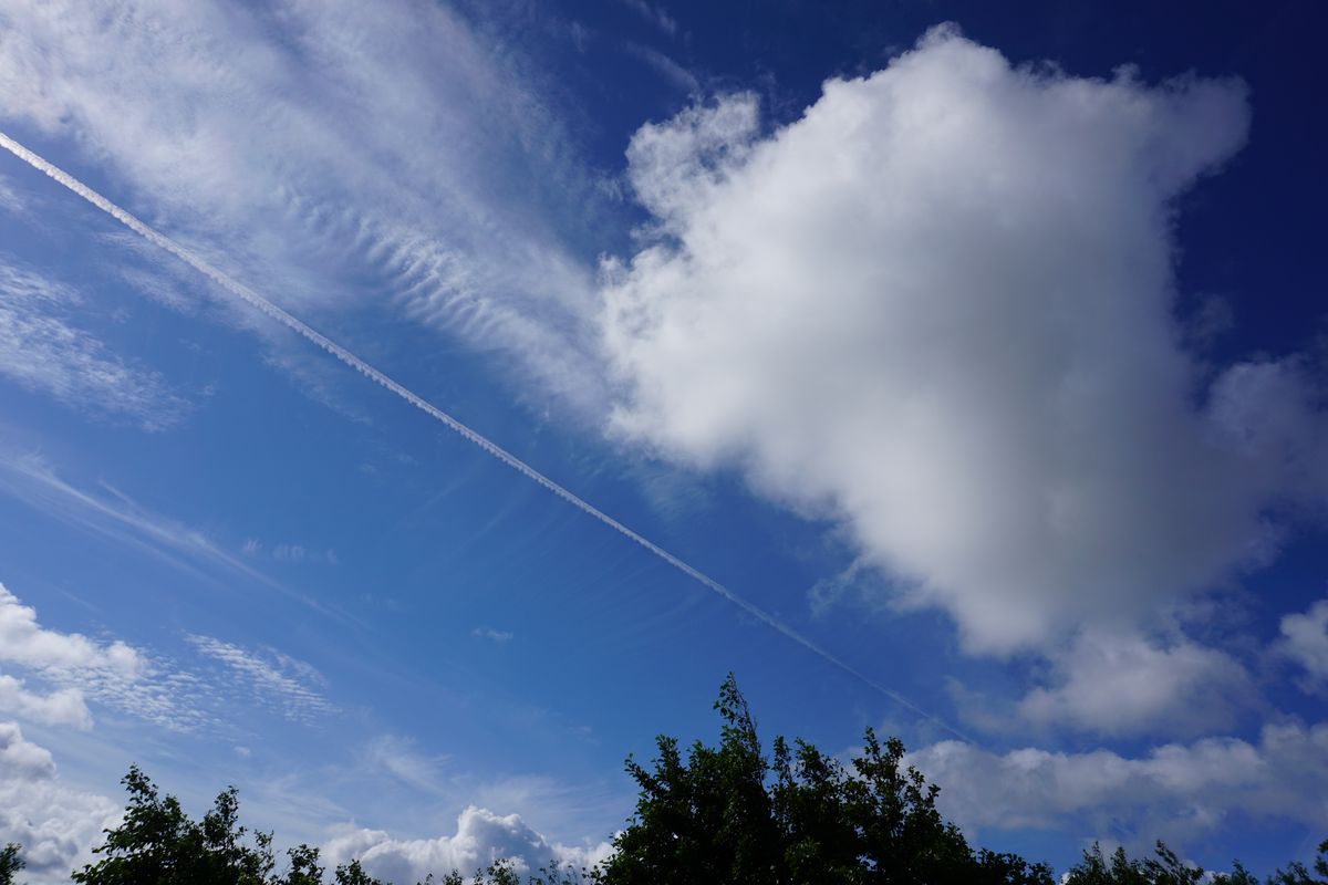 enlarge the image: Neben einer Cumuluswolke sind die hohen Eiswolken, die Zirren zu sehen. Darunter ist auch eine linienförmige Zirruswolke, ein Kondensstreifen von einem Flugzeug. 