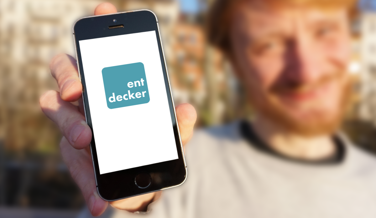 zur Vergrößerungsansicht des Bildes: Ein junger Mann hälte ein Smartphone mit der Aufschrift Entdecker-App in die Kamera. Foto: Universität Leipzig