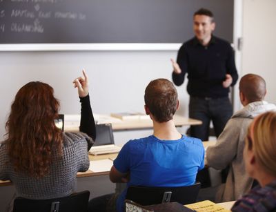 Hochschullehrer steht vor Studierenden an einer Tafel, eine Studentin meldet sich, Foto: Colourbox