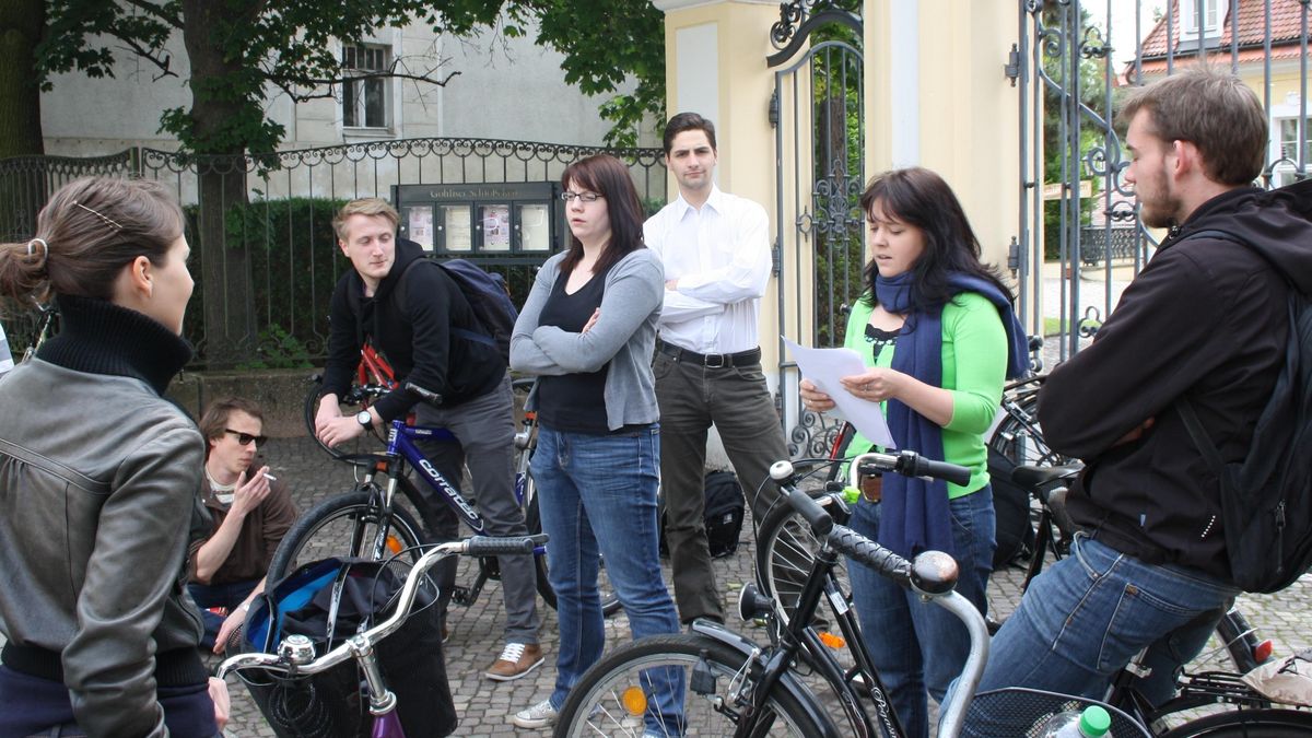 zur Vergrößerungsansicht des Bildes: Eine Gruppe junger Menschen auf Rädern hört einer jungen Frau bei einem Vortrag zu.