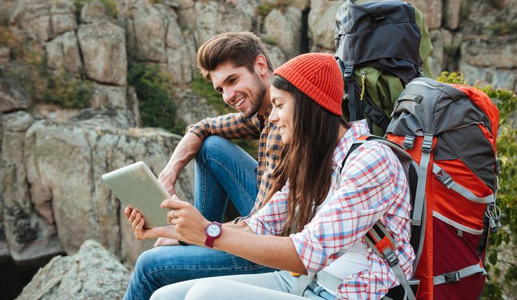 Ein Mann und eine Frau sitzen in den Bergen und schauen auf ein Tablet. Foto: Colourbox