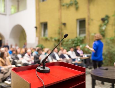 In einem Innenhof sitzen viele Menschen vor einem Stehpult im Vordergrund. Foto: Colourbox