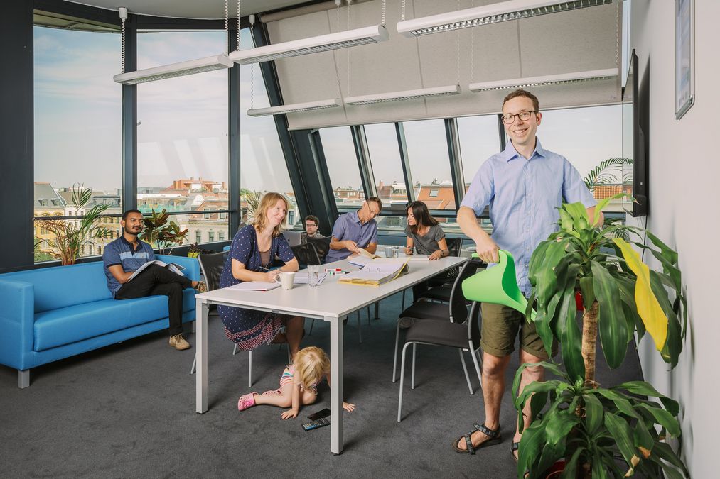 zur Vergrößerungsansicht des Bildes: Die Mitarbeiterinnen und Mitarbeiter der Arbeitsgruppe sitzen im Foyer am Tische und arbeiten. Foto: Stephan Flad