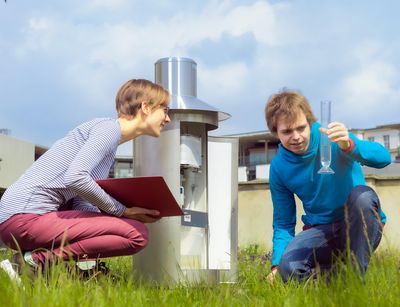 Zwei Studierden sitzen auf der Wetterwiese. Ein Studierender hät einen Glaszylinder hoch und eine Studierende liest ab. Foto. Swen Reichhold