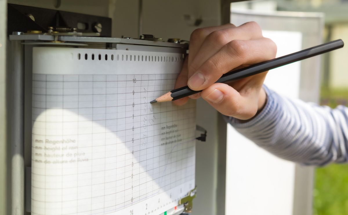 enlarge the image: On the opened rain gauge, a hand writes data on the measuring sheet. Photo: Swen Reichhold