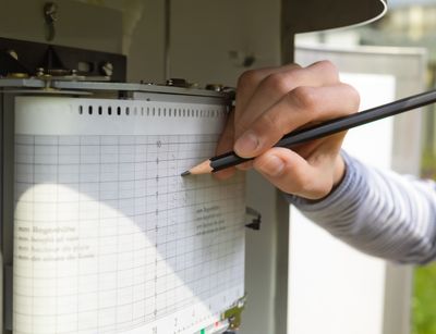 Auf dem geöffneten Regenmesser schreibt eine Hand Daten auf das Messblatt. Foto: Swen Reichhold
