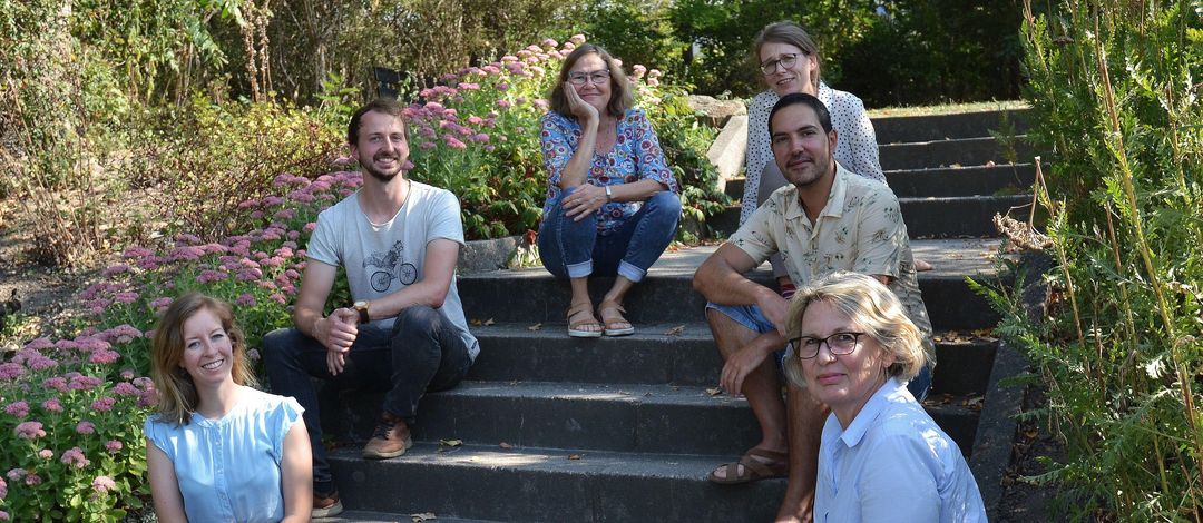 Eine Gruppe von sechs Wissenschaftlern und Wissenschaftlerinnen sitzt auf einer Treppe, umgeben von Grün. 
