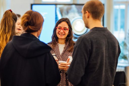 Frau, die eine Tasse hält, unterhält sich lächelnd in einer Gruppe von Menschen