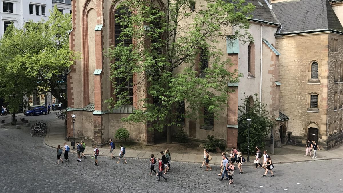 zur Vergrößerungsansicht des Bildes: Der Blick richtet sich aus der Vogelperspektive auf eine Gruppe von Menschen, die sich über den Nikolaikirchhof bewegt.